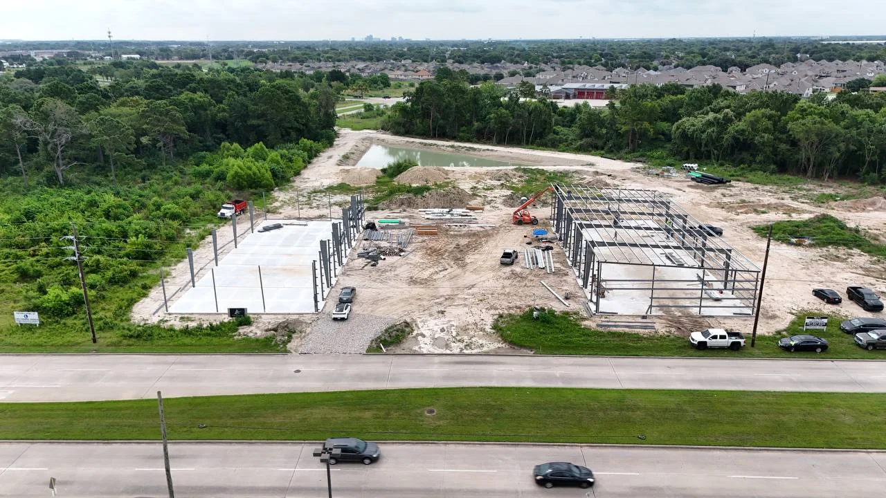 Bammel Business Park Phase 1 aerial, 7 July 2026 (Day 128): PEMB structural steel erection underway — the first building's steel frame is up over the cast slabs, 12902 Bammel N Houston Rd, Houston TX 77066